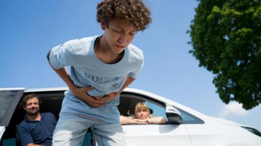 Junge steht am Straßenrand und hält sich den Bauch