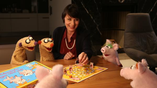 Die Gräfin (Ute Willing) spielt mit den Erdmännchen und den Ferkeln „Schweinchen ärger Dich nicht“. | Rechte: NDR/bigSmile