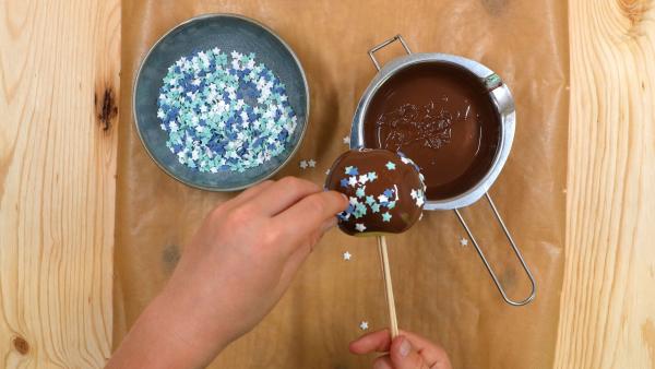 Kinderhände streuen auf einen Schoko-Apfel bunte Sterne