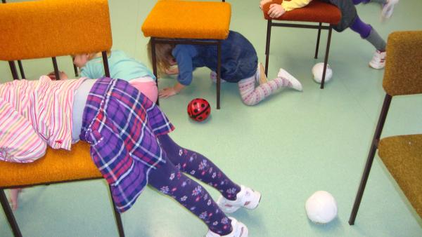 Die Kinder kriechen abwechselnd unter den Stühlen durch und klettern darüber.