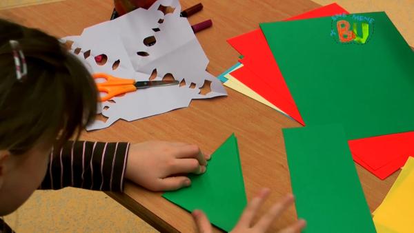 Sophie faltet ein grünes Blatt Papier in der diagonale.