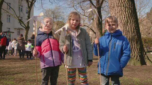 Nora, Charlotte und Maxim zeigen ihre gebastelten Steckfriedenstauben aus Papier. 