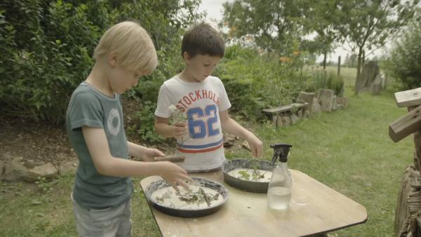 Zwei Kinder backen einen Blumenkuchen im Garten