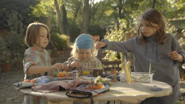 Drei bastelnde Kinder an einem Tisch im Garten. 