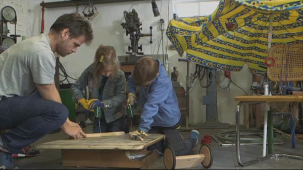 Zwei Kinder bohren mit der Hilfe eines Erziehers auf Holz.
