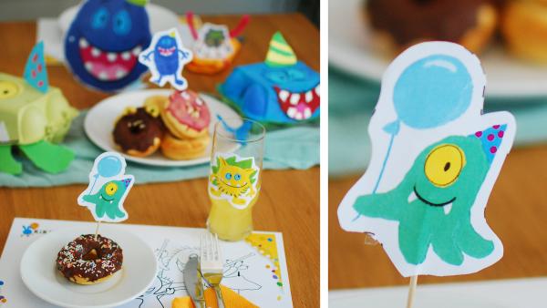 Monsterarty Dekorationsidee für Druckvorlagen von Kikaninchen. in Monster Caketopper in einem Donut verziert mit Schokolade und Streuseln auf einem reichlich gedeckten Tisch mit Monsterbildern für eine Monsterparty mit Kindern 