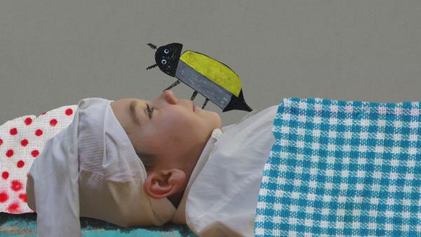 Ein Junge als Onkel Fritz verkleidet liegt mit seiner Schlafmütze im Bett. Auf seiner Nase krabbelt ein großer Maikäfer aus Papier. | Rechte: KiKA