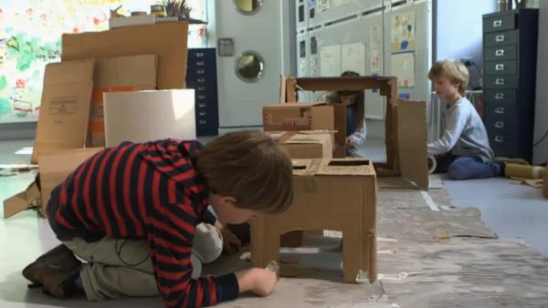 Drei Kinder bauen aus alten Pappkartons eine kleine Wohnung nach mit einem Herd und einem Kühlschrank. | Rechte: KIKA