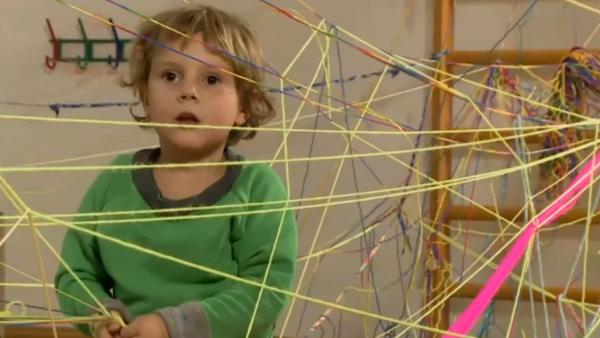 Als Beschäftigungsidee hat ein Kind bunte Fäden kreuz und quer durch einen Raum gezogen und verknotet. Es sieht aus wie ein großes Spinnennetz. | Rechte: KIKA