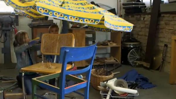 Upcycling-Idee für Kinder: Zwei Kinder bauen aus alten Stühlen, einem kaputten Sonnenschirm und anderen alten Gegenständen eine neue Maschine. | Rechte: KiKA