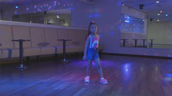Ein Mädchen tanzt in einer Tanzschule den "Rumpelstilzchentwist". Der Tanzsaal ist wie in einer Disko beleuchtet. | Rechte: KiKA