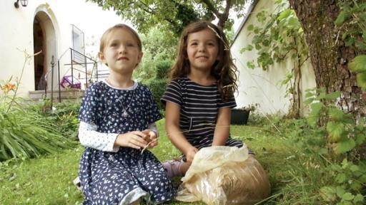 Zwei Vorschulkinder sitzen im Gras. Vor ihnen steht eine Plastiktüte mit Ton.