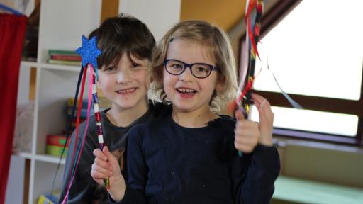 Zwei Vorschulkinder halten lachend ihre selbstgebastelten Zauberstäbe hoch.