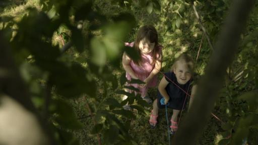 Zwei Mädchen stehen zwischen gespannten Schnüren und blicken nach oben in einen Baum.