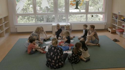 Ein Mädchen sitzt mit anderen Kindern im Kreis auf dem Boden. Sie gucken sich neugierig Bilder an.