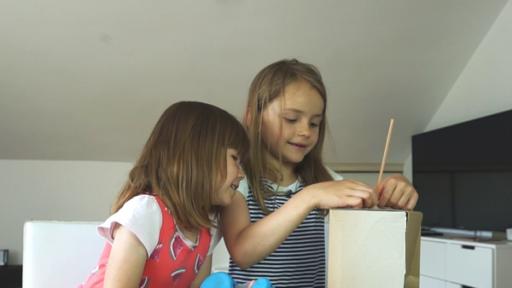 Zwei Vorschulkinder sitzen an einem Tisch mit Bastelutensilien und beugen sich über einen Karton.