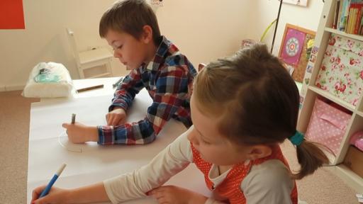 Ein Junge und ein Mädchen sitzen an einem Tisch im Kinderzimmer. Sie malen gemeinsam ein Bild.