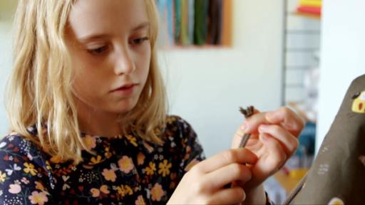 Ein Mädchen schaut konzentriert ihren selbstgenähten Turnbeutel an. In der Hand hält sie ein Seil.