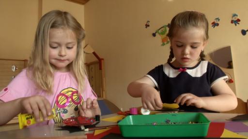 Lena uns Astrid sind vertieft in ihre Bastelarbeiten. Sie kleben bunte Steine auf Papier.