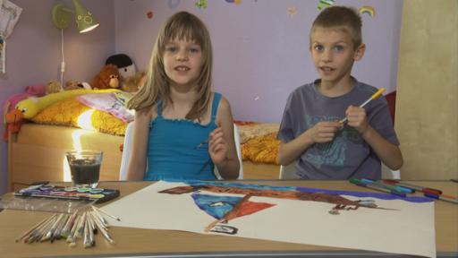 Links sitzt ein Mädchen mit einem Pinsel in der Hand. Rechts ein Junge mit einem Stift. Beide sitzen am Schreibtisch.