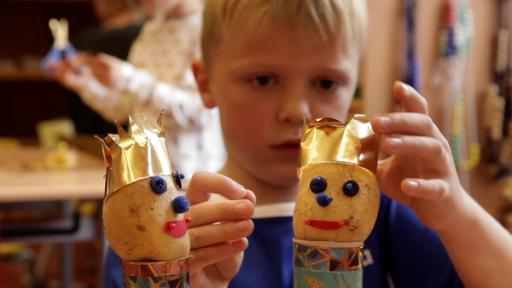 Vor einem Jungen steht eine Figur, die er aus einer Kartoffel gemacht hat. Sie trägt eine Krone.