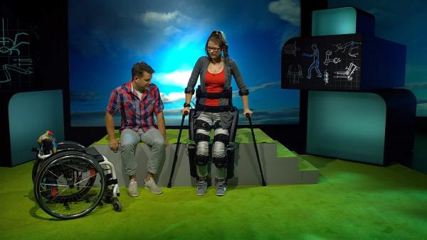 Nicole zeigt Felix, was sie mit ihrem Exoskelett alles kann. Sie kann damit - trotz Lähmung - laufen. | Rechte: KiKA