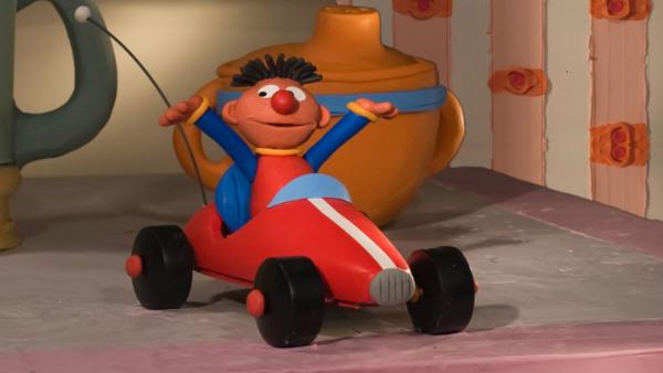 Ernie hat großen Spaß im ferngesteuerten Spielzeugauto, mit dem er über den Tisch rasen kann. | Rechte: NDR/Sesameworkshop