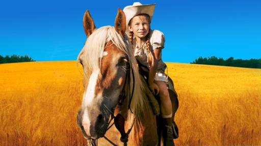 In einem goldgelben Getreidefeld vor strahlend blauem Himmel steht das Pferd Mississippi mit Emma (Zoë Charlotte Mannhardt) auf dem Rücken.