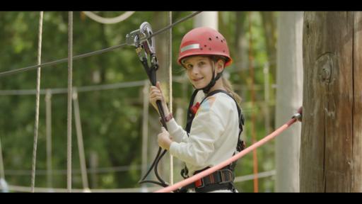 Eileen steht auf einer Kletterplattform. Sie ist mit Seilen gesichert und trägt einen Helm.