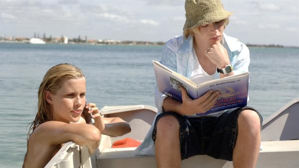 Lewis (Angus McLaren, li.) studiert ein Buch mit mystischen Seewesen, während Emma (Claire Holt) als Meerjungfrau im Meer unterwegs ist. | Rechte: ZDF/Jasin Boland
