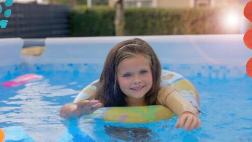 Maya schwimmt mit Schwimmreifen in einem Schwimmbecken. Sie streckt ihren Arm nach vorne ins Wasser aus und lächelt.