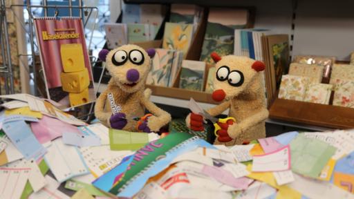 Zwei Erdmännchen aus Stoff sitzen hinter einem Papierberg aus zerschnittenen Kalendern. Beide haben eine Schere in der Hand. 