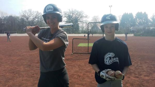 Auf einem Baseball-Feld hält Jess (links) einen Baseball-Schläger und trägt einen Helm. Neben ihr steht Pit, ebenfalls mit Helm. Er trägt einen Baseball-Handschuh und hält zwei Bälle.