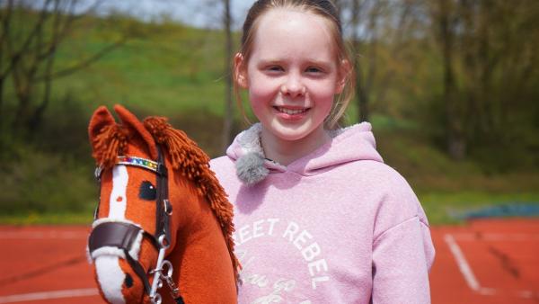 Die zwölfjährige Emily ist ein Riesenfan von Hobby Horsing. Sie trägt einen rosa Kapuzenpullover und hält das Steckenpferd in der Hand.