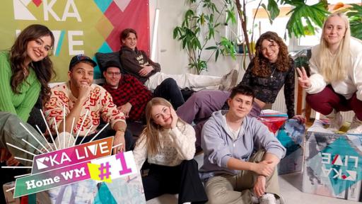 Von links nach rechts sitzen Sarah, Malik Harris, Ben, Nevio Wendt, Laila Ziegler, Marco Strecker, Luana Knöll und Maria Ziffey auf und vor einem Sofa. Unten links steht "Home WM #1".