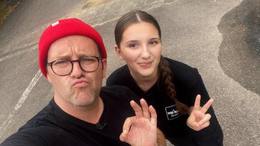 Ben, mit Mütze und Brille, macht ein Foto aus Selfie-Perspektive. Er zeigt das "Alles in Ordnung" Handzeichen. Neben ihm steht Mihaela. Sie hat einen geflochtenen Zopf und zeigt das Victory-Zeichen.