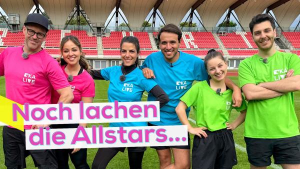 Die KiKA LIVE Allstars 2024 stehen in den jeweiligen Teams nebeneinander auf einem Sportplatz. V.l.n.r.: Team Pink mit Ben und Sarah, Team Blau mit Clari und Sherif und Team Grün mit Marina und Tarkan. Aufschrift unten links: Noch lachen die Allstars...