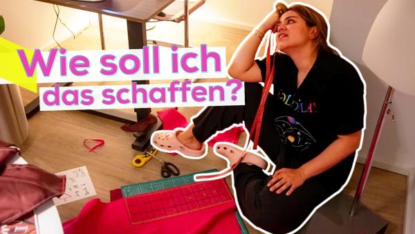 Sarah sitzt auf dem Boden an die Wand gelehnt. Sie sieht geschafft und etwas verzweifelt aus. Auf dem Boden rund um sie herum liegen roter Stoff und Stoffreste, eine Schneidmatte, eine Schere und Skizzen. Im Hintergrund angeschnitten eine Schneiderpuppe und ein Tisch mit einer Nähmaschine. Aufschrift obere, linke Bildhälfte: Wie soll ich das schaffen?