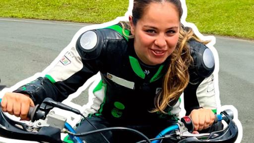 Rechts Sarah in Motorradbekleidung. Sie sitzt nach vorn gebeugt auf einem Motorrad mit den Händen am Lenker und schaut freudig. Im Hintergrund die Kurve einer Rennstrecke mit drei Motorrädern bei einem Rennen. Aufschrift unten links: Meistert sie die Maschine?