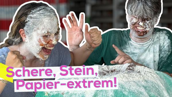 Sarah und Lukas mit den Gesichtern und Haaren voll Matsch aus Mehl, Schokosoße und Ketchup. Beide lachen herzlich. Direkt vor ihnen ein Kissen, dass auch voll Mehl und Matsch ist. Aufschrift unten links: Schere, Stein, Papier - extrem.