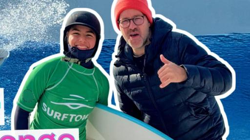 Rechte: KiKA/Andrea Thoben Fabiana im Surfanzug mit ihrem Surfbrett unter den Arm geklemmt. Dicht neben ihr steht Ben mit lässiger Handgeste. Im Hintergrund ein Bild von Fabiana beim Wellenreiten. Links die Aufschrift Surf-Challenge.
