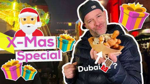 Ben hält eine Tüte mit Churros in der Hand und schaut dabei sehr zufrieden. Ein Grafik-Pfeil mit dem Text Dubai und ein Schoko-Emoji mit Fragezeichen zeigt auf dieses spanische Gebäck. Um Ben herum Geschenke und ein Weihnachtsmann-Emoji. Aufschrift links: X-Mas Special. Im Hintergrund ein Weihnachtsmarkt.