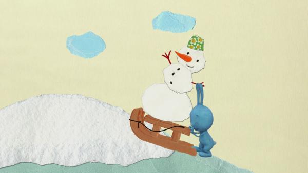 Kikaninchen schiebt einen Schneemann auf einem Schlitten