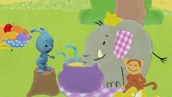 Ein Affe, ein Elefant und Kikanichen sitzen auf einer Picknickdecke.