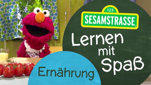 Elmo steht in der Küche und trägt ein Lätzchen mit seinem Namen, neben ihm, auf einem Schild, steht: "Sesamstraße: Lernen mit Spaß - Ernährung".