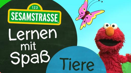 Elmo steht neben einem Schild auf dem steht: "Sesamstraße: Lernen mit Spaß - Tiere".