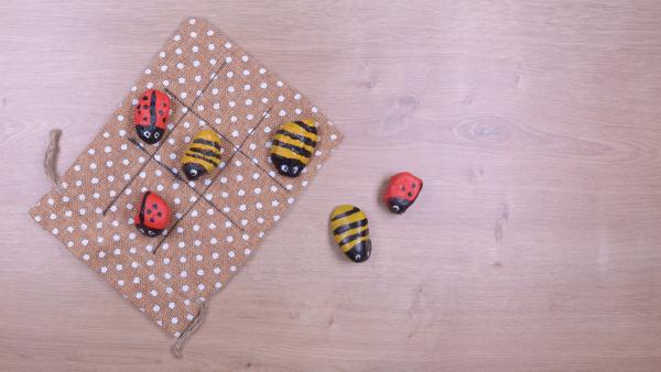 Steine als Marienkäfer und Bienen bemalt liegen auf einer Spielfläche | Rechte: KiKA
