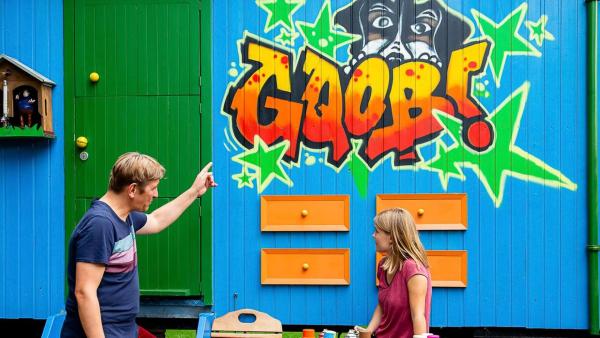 Fritz zeigt auf die Bauwagenwand, auf der ein Graffiti gesprüht wurde. Ein Mädchen steht davor. | Rechte: ZDF