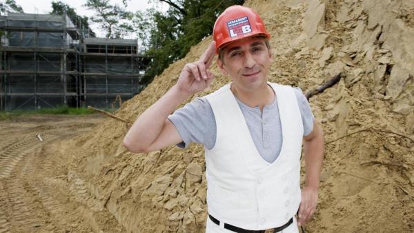 Fritz steht in Dachdeckerkleidung mit Bauhelm auf einer Baustelle. | Rechte: ZDF