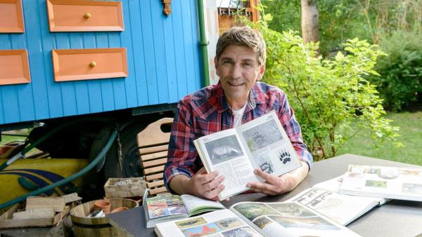 Fritz Fuchs sitzt vor dem Bauwagen mit einem Buch über Dachse | Rechte: ZDF